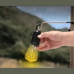 Portable LED camping bulb with a black top hanging from a hook, held in a hand outdoors
