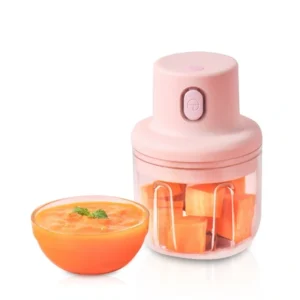 Pink rechargeable garlic chopper with chopped vegetables in its clear bowl beside a bowl of puree