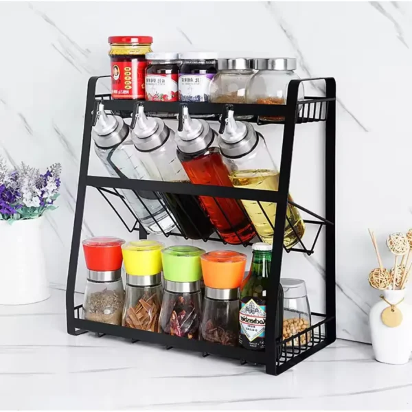 Black three-tier kitchen rack with spice jars and tilted bottle shelves on a white marble background