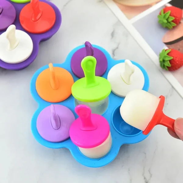 Blue 7-cavity silicone popsicle mold with coloured stick lids and a popsicle being lifted out