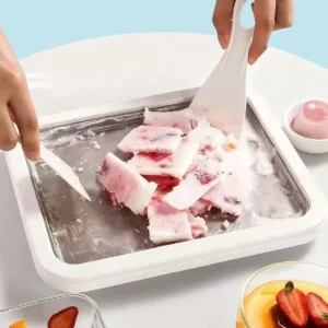 Spade scraping frozen yogurt pieces on a white ice cream plate with fruit nearby
