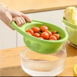 Hand tilting a green colander basket of tomatoes over a clear bowl
