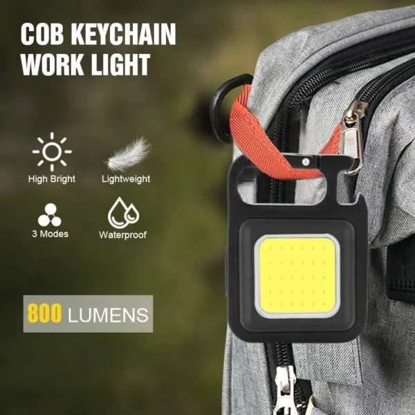 Mini LED flashlight keychain clipped to the strap of a grey backpack