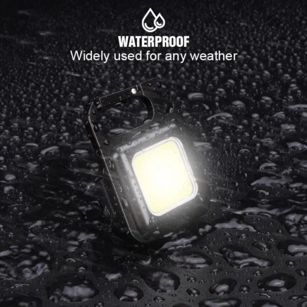 Mini LED flashlight keychain glowing on a wet surface covered in water drops