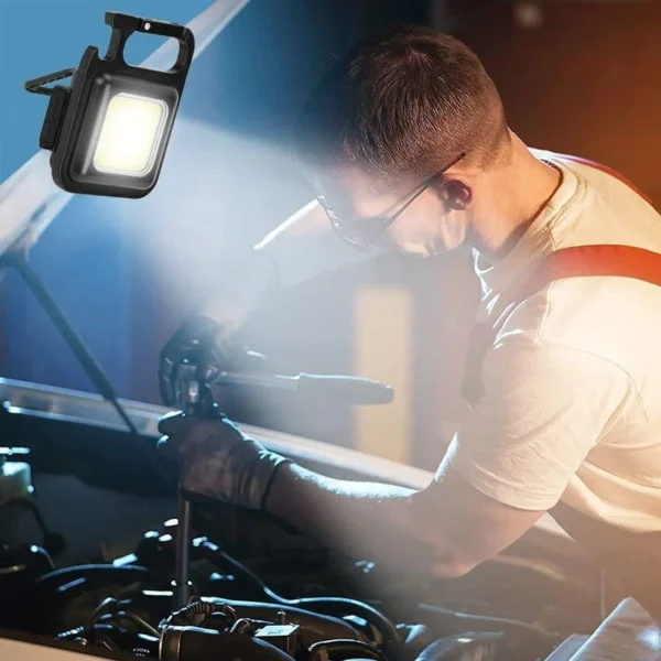 Mini LED flashlight keychain lighting the engine bay while a man works on a car