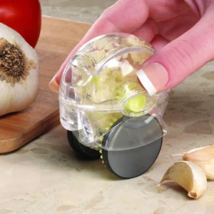 Hand rolling a clear garlic mincer with a black wheel on a board beside garlic cloves