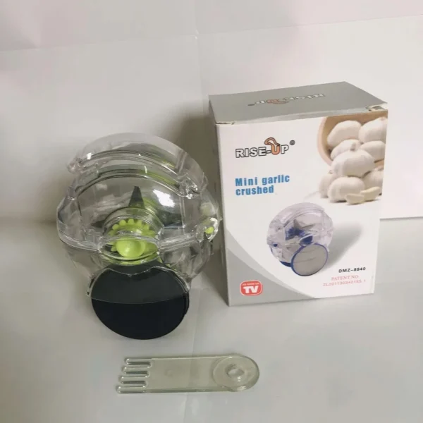 Garlic mincer unit next to its retail box and a small plastic tool