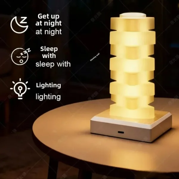 Stacked lamp glowing warm yellow on a bedside table beside a glass