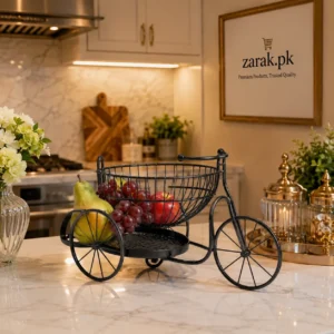 Black tricycle-shaped wire fruit basket holding a pear, grapes and an apple on a marble counter